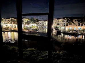 A nighttime view of a waterfront area with buildings, a dock, and a calm water body reflecting lights.