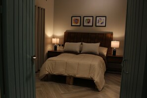 Una cama bien tendida con un cabecero de madera, dos lámparas de noche y tres cuadros en la pared.