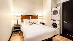 Un lit bien fait, avec une tête de lit, deux lampes de chevet, une table de chevet et un lave-linge fixé au mur.