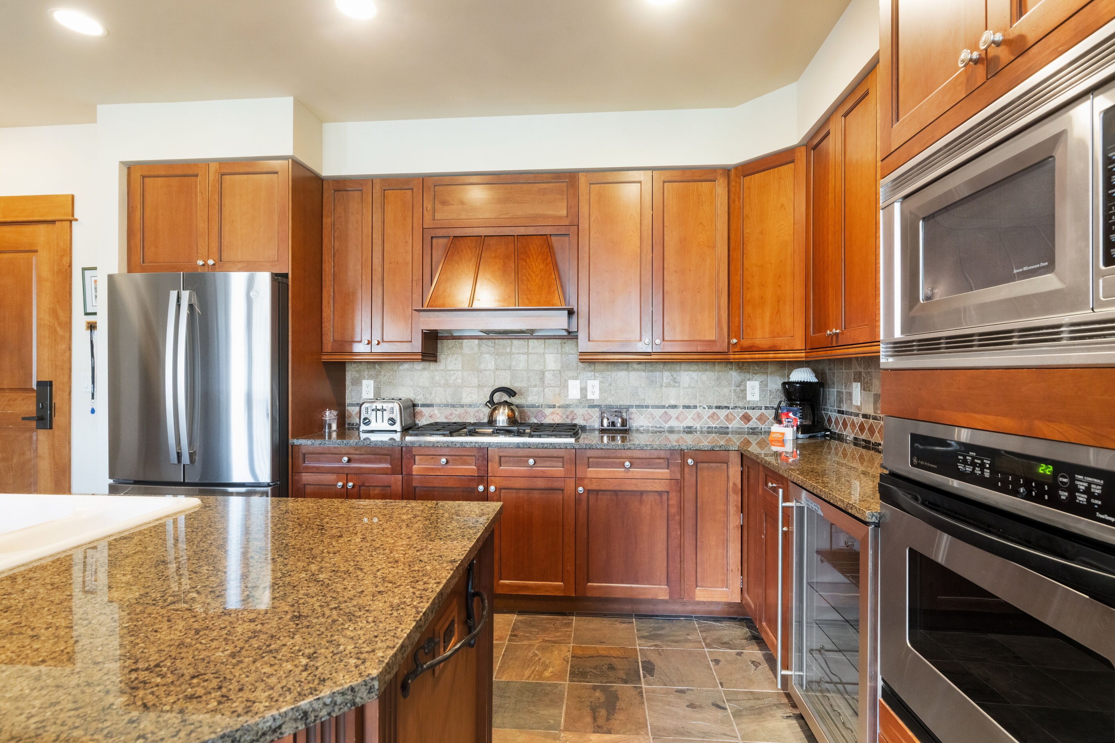 A modern kitchen with wooden cabinets, stainless steel appliances, and a granite countertop.