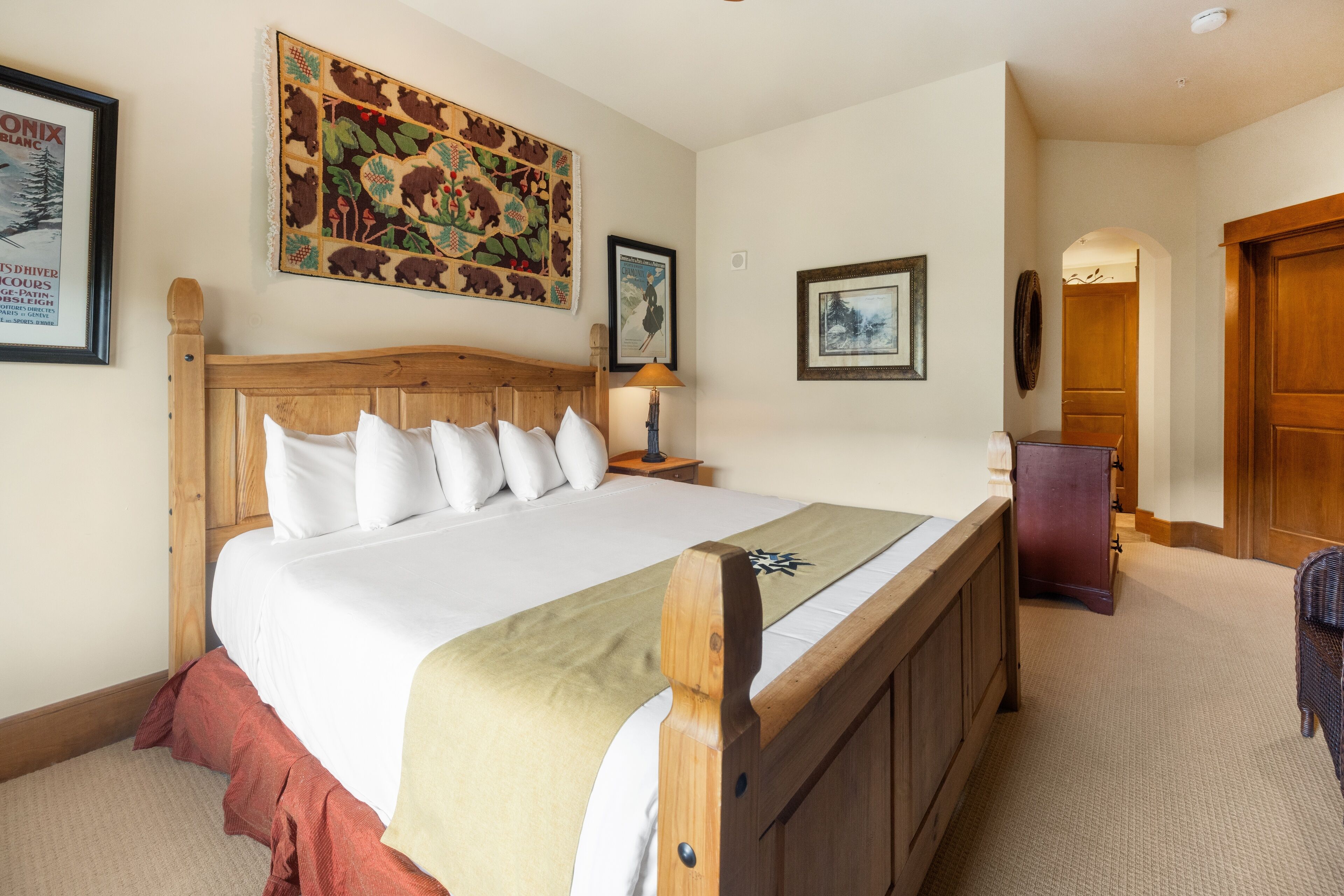 A neatly made bed with a wooden headboard, a red skirt, and a beige throw blanket.