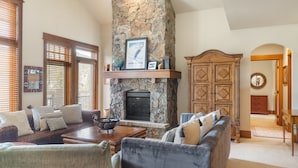 A living room with a stone fireplace, wooden furniture, and a view of the dining area. - 3br Ski-in/ski-out~on Mountain~lone Eagle 3053 3 Bedroom Condo by RedAwning (Keystone)
