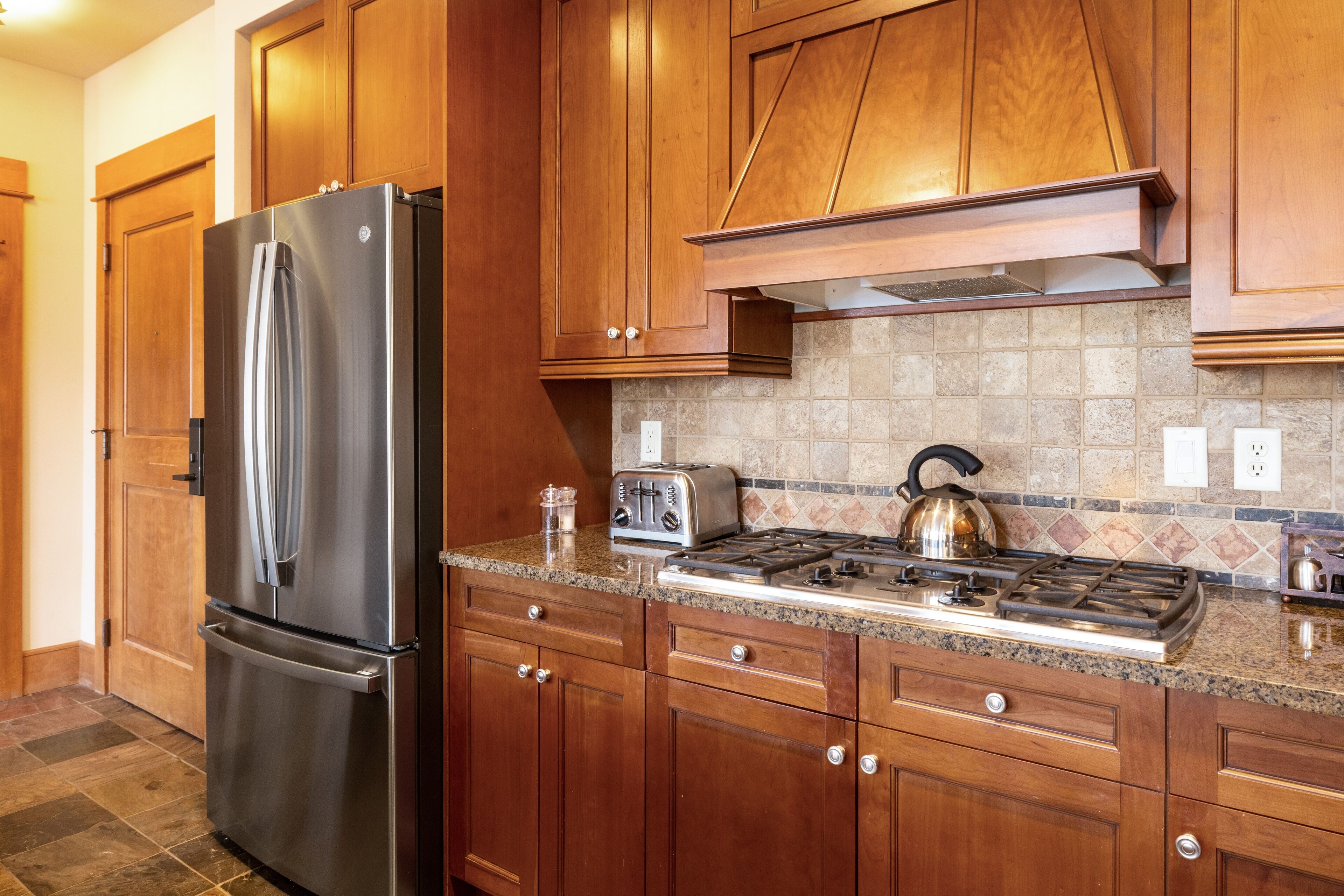 A kitchen with wooden cabinets, a stainless steel refrigerator, a gas stove, and a toaster.