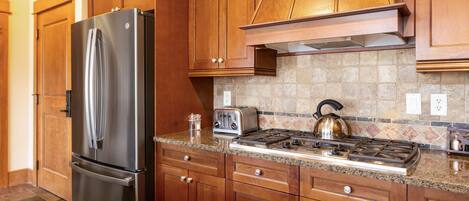 A kitchen with wooden cabinets, a stainless steel refrigerator, a gas stove, and a toaster.