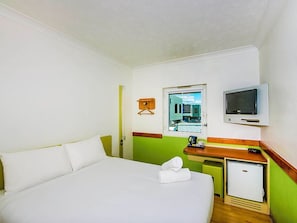 A hotel room with a bed, a small desk, a television, and a window with a view of buildings. - Imperial Motel Windsor (Windsor)
