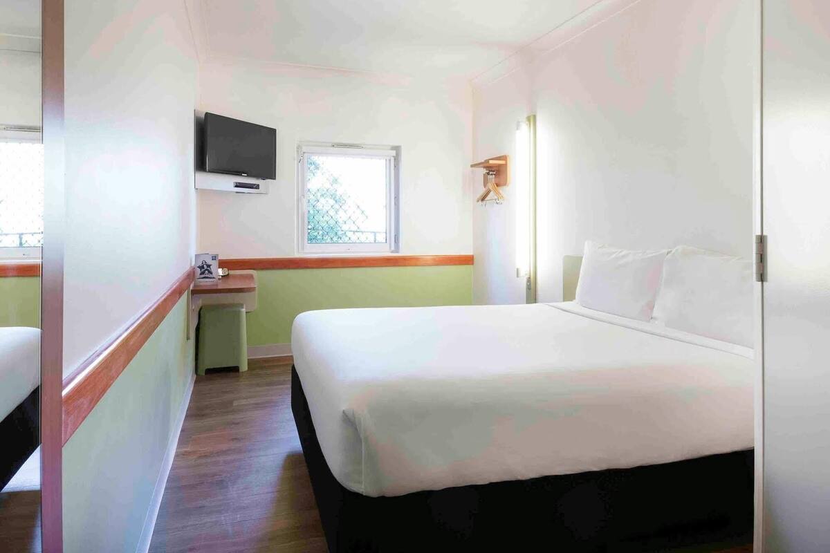 Hotellihuone, jossa on sänky, televisio, ikkuna ja pieni työpöytä.