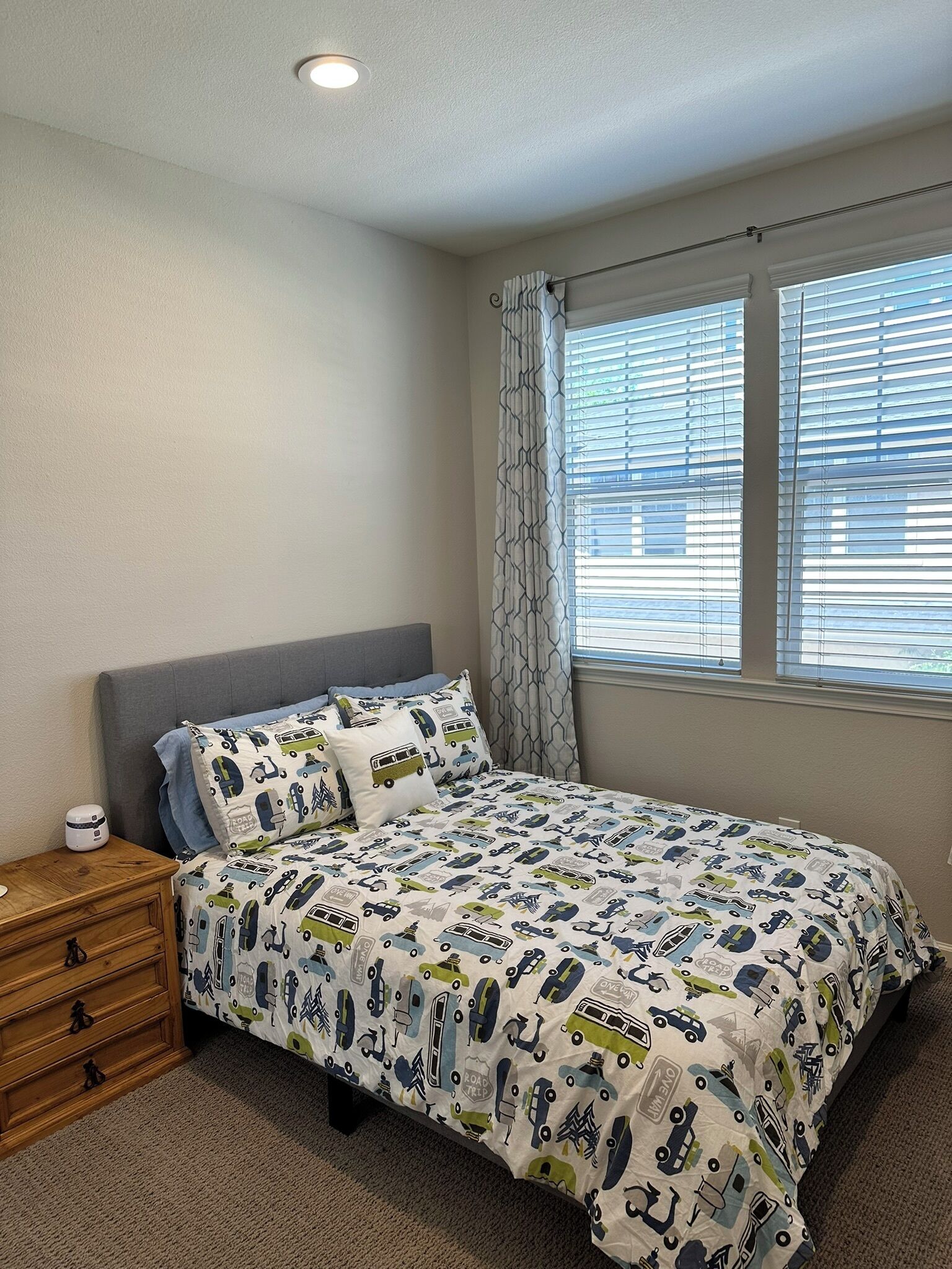 Quarto com cama, mesa de cabeceira, cômoda e janela com persianas.