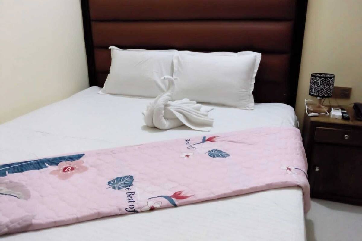 A neatly made bed with white linens, a pink floral blanket, and a white towel folded into a swan shape.