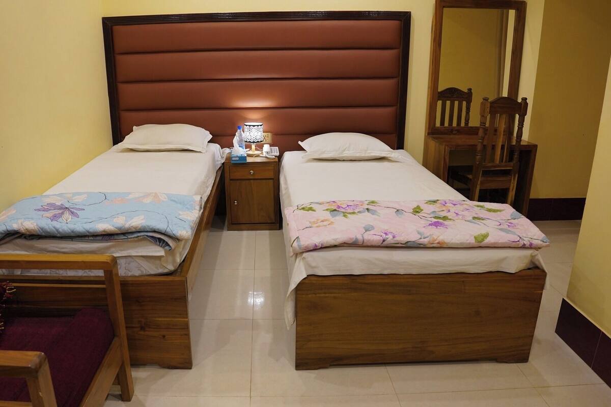 A double room with two single beds, a wooden nightstand with a lamp, a chair, and a mirror on the wall.