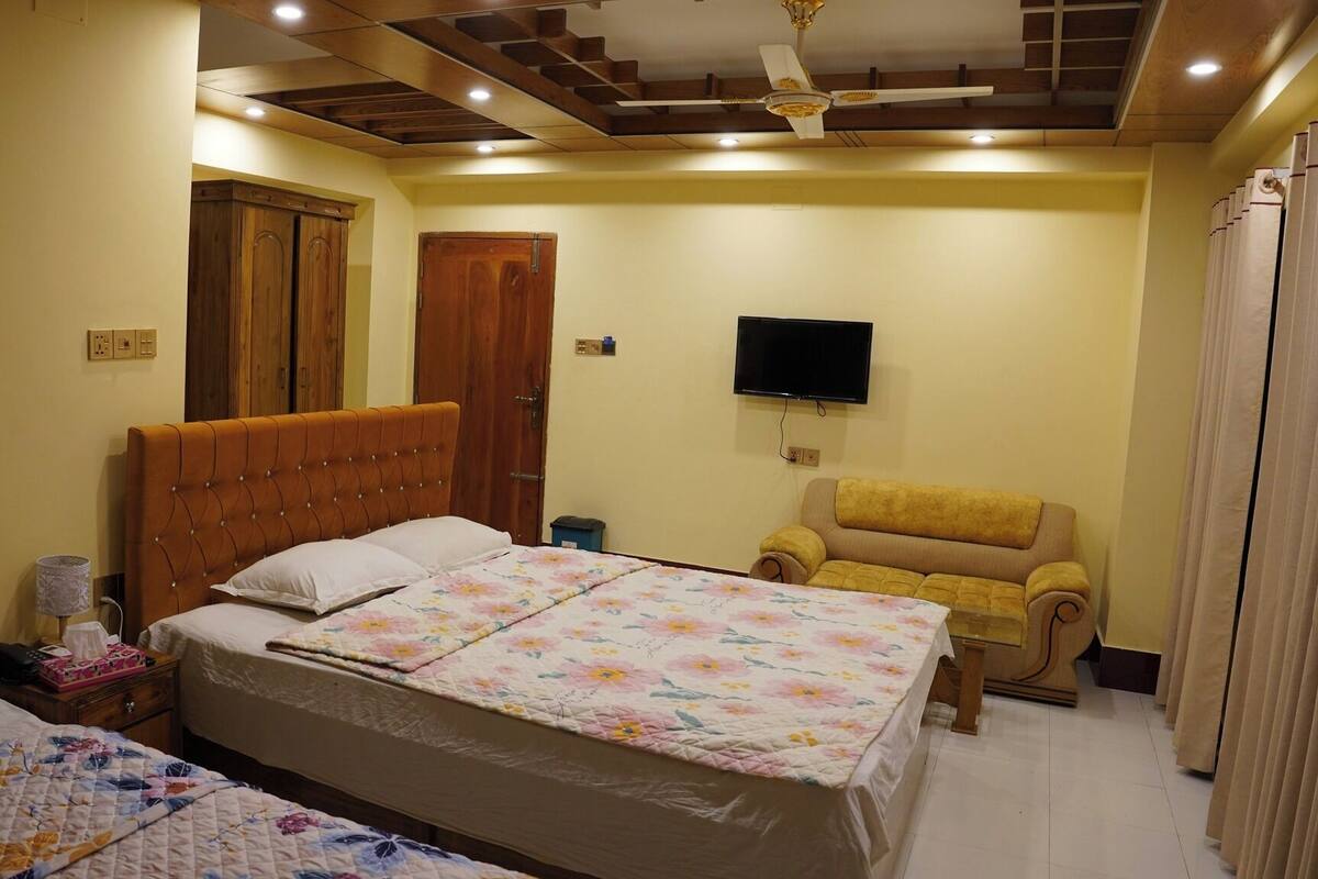 A bedroom with a large bed, a sofa, a TV, and wooden wardrobes.