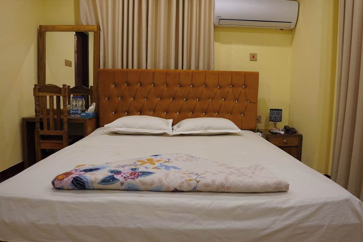 A neatly made bed with a floral bedspread, a wooden headboard, and a bedside table with a lamp and a phone.