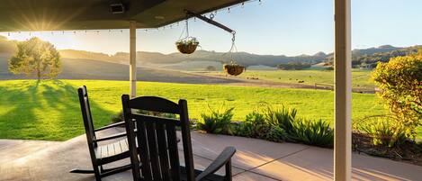 A covered patio with two rocking chairs facing a scenic view of a green field and hills.