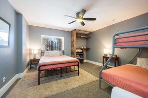 A bedroom with a bunk bed, a desk, a chair, a window with a view of buildings, and a ceiling fan.