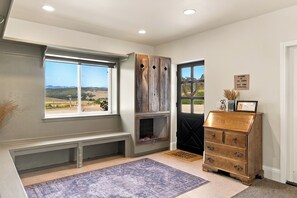 A room with a large window, a fireplace, a bench, a dresser, and a rug.