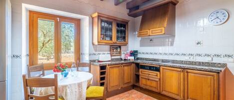Una cocina con armarios de madera, salpicadero de azulejos blancos, un reloj y un comedor con mesa y sillas.