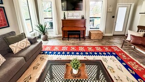 A living room with a piano, a sofa, a coffee table with a plant, and a colorful rug. - 4BR Sleeps 12 - Hottub Firepit - 1 Mile to Lake & River! (Canyon Lake)
