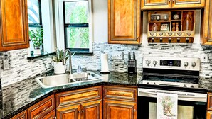 A kitchen with wooden cabinets, a stainless steel sink, a stove, and a window with a view of greenery. - 4BR Sleeps 12 - Hottub Firepit - 1 Mile to Lake & River! (Canyon Lake)