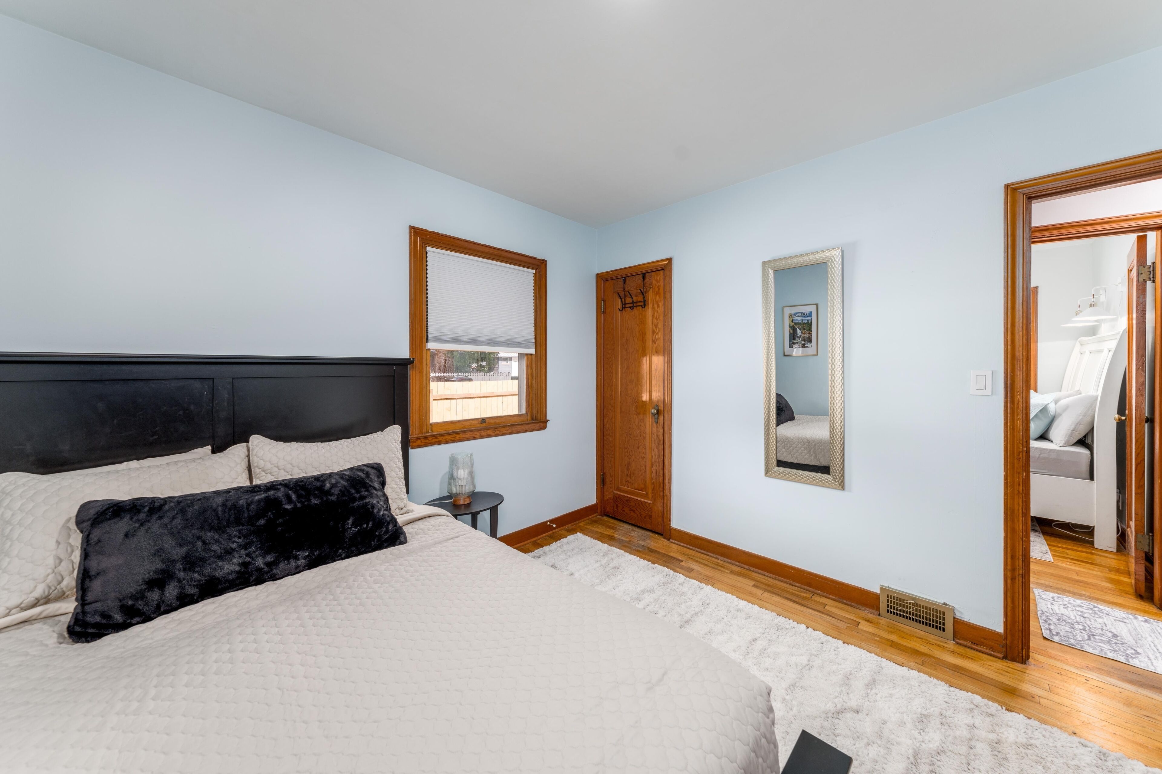 A bedroom with a bed, a wooden door, a mirror, and a window.