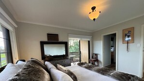 A bedroom with a large bed, a flat-screen TV, a ceiling light, and a view of the outdoors. - Brum's Place | Inner City Tropical Haven (Maribyrnong)