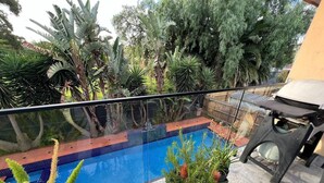 A rooftop pool with a glass balustrade, surrounded by tropical plants and a wooden fence. - Brum's Place | Inner City Tropical Haven (Maribyrnong)