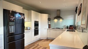 A modern kitchen with white cabinetry, a black refrigerator, a built-in oven, and a stainless steel range hood. - Brum's Place | Inner City Tropical Haven (Maribyrnong)