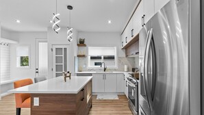 Une cuisine moderne dotée d’un îlot central, d’appareils électroménagers en acier inoxydable et d’un plancher en bois.