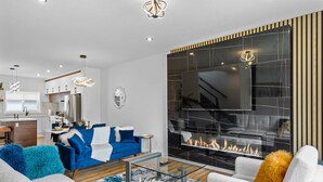 Un salon moderne avec une cheminée, une cuisine en arrière-plan et un coin repas.