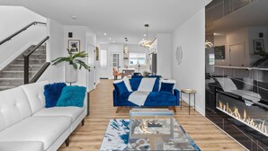Un salon moderne avec un canapé blanc, des fauteuils bleus, une table basse en verre et une cheminée.