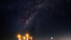 Paisaje desértico nocturno con una persona de pie a lo lejos y una estructura iluminada en primer plano.