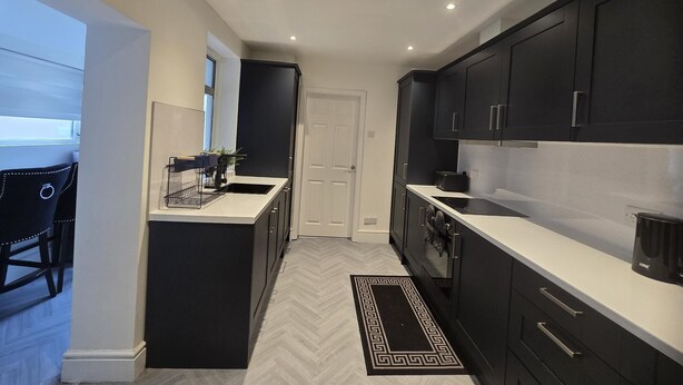 Une cuisine moderne avec des meubles de couleur sombre, un plan de travail blanc et un sol à motifs en chevrons.