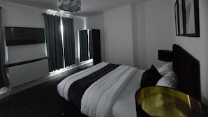 Une chambre d’hôtel moderne avec un grand lit, une table de chevet, un radiateur, une fenêtre avec des rideaux et un téléviseur fixé au mur.