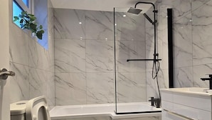 Une salle de bain moderne avec une douche à parois de verre, des toilettes blanches et un tapis noir.