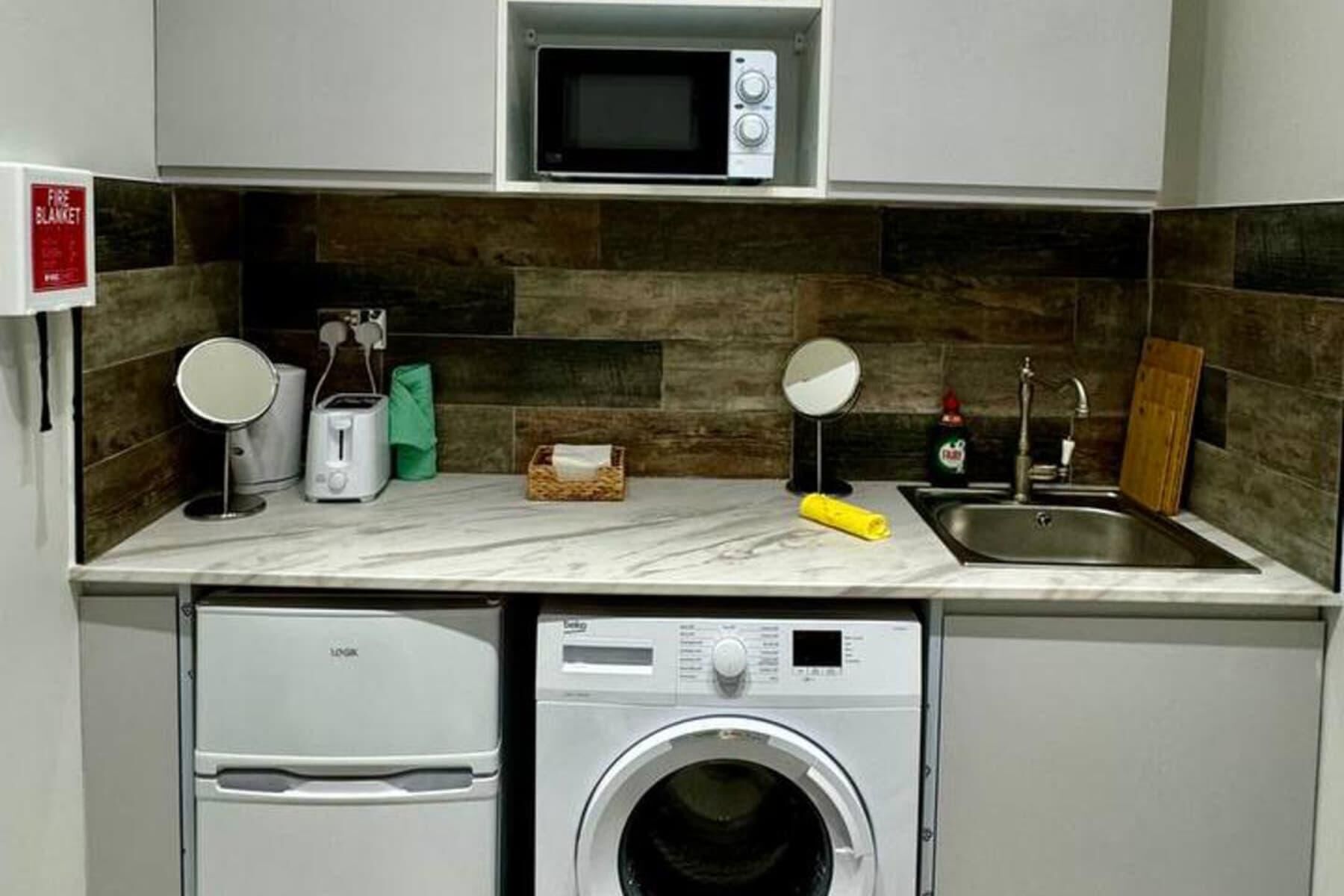 Une cuisine compacte équipée d’un four à micro-ondes, d’un grille-pain et d’un lave-linge.