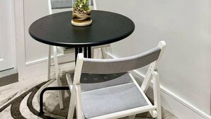 Un tavolo da pranzo rotondo con piano in vetro e una sola sedia con seduta e schienale grigio imbottiti.