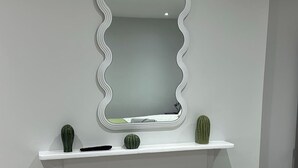 Un bagno con un mobile lavabo bianco, uno specchio con cornice ondulata e due vasi decorativi sullo scaffale.