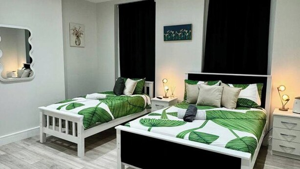 Una camera moderna con due letti singoli, un comodino con una lampada, uno specchio e un quadro appeso al muro.