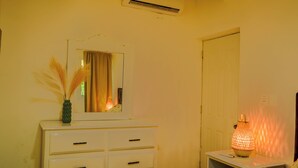Une chambre avec une commode blanche, une table de chevet avec une lampe et une porte.