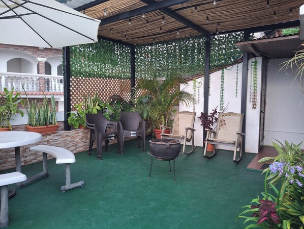 Eine Terrasse im Freien mit grünen Bodenplatten, Korbmöbeln und Blumentöpfen.