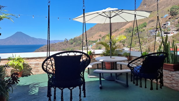 Eine Terrasse mit Hängestühlen, einem Tisch und einem Sonnenschirm mit Blick auf die Küste und einem Berg in der Ferne.