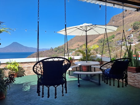 A patio with hanging chairs, a table, and an umbrella overlooking a coastal view with a mountain in the distance.. Casa Bella Vista, Cerca de Panajachel