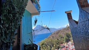 Ein Gebäude mit blauer Fassade, einem begrünten Balkon und Blick auf Meer und Hügel im Hintergrund.