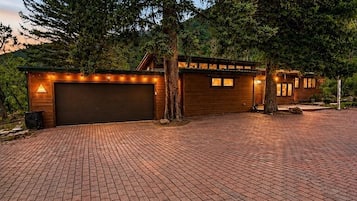 A two-story building with a garage, paved driveway, and a large tree in front.