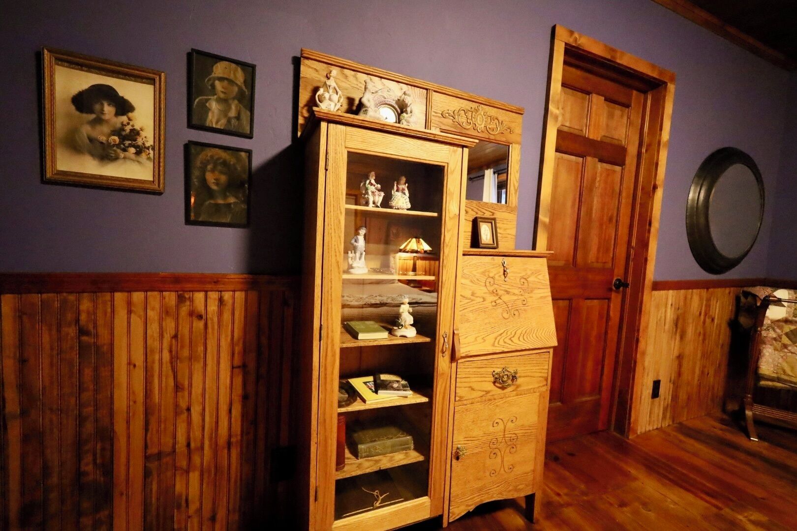 Ein Zimmer mit einem Holzschrank an einer violetten Wand, Holzvertäfelung an den Wänden und einem Spiegel auf der rechten Seite.