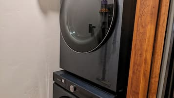 A stacked washer and dryer unit with a metallic vent cover above.