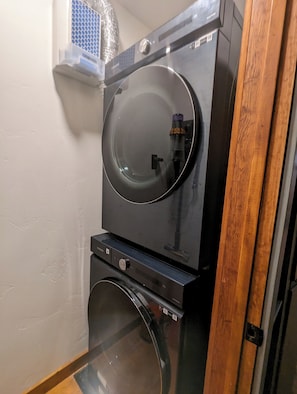 A stacked washer and dryer unit with a metallic vent cover above. - Expect! WOW! Jacuzzi, Game Room, Fire Pit, Waterbed, Massage Chair, Remodel 2024 (Glenwood Springs)