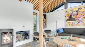 Un salon moderne avec une cheminée, des poutres apparentes en bois au plafond, un canapé et une table à manger.
