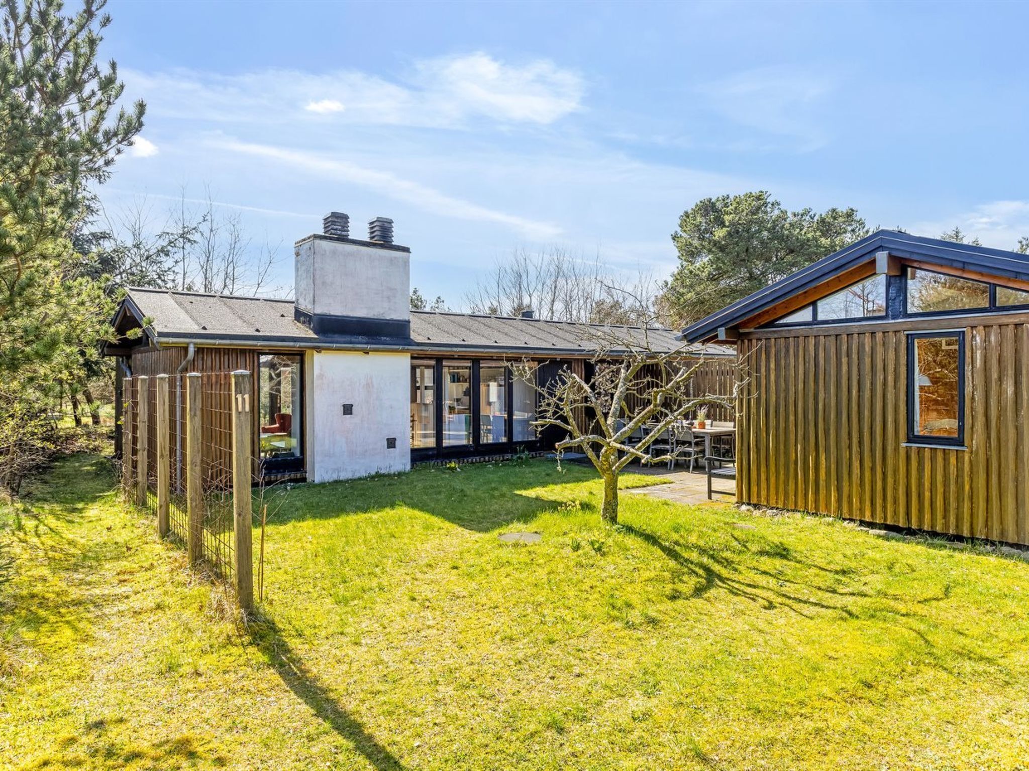 Et moderne hus med en stor glasudvidelse, en træterrasse og en indhegnet have.
