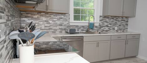 A modern kitchen with grey cabinets, a tiled backsplash, a window, and a dishwasher.