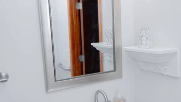 Ein Badezimmer mit einem weißen Waschbecken, einem Spiegel mit Holzrahmen und einer Leuchte darüber.