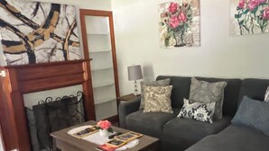 Una sala de estar con un sofá gris oscuro, una mesa de centro de madera con un jarrón y libros, una alfombra estampada y un ventilador de techo.